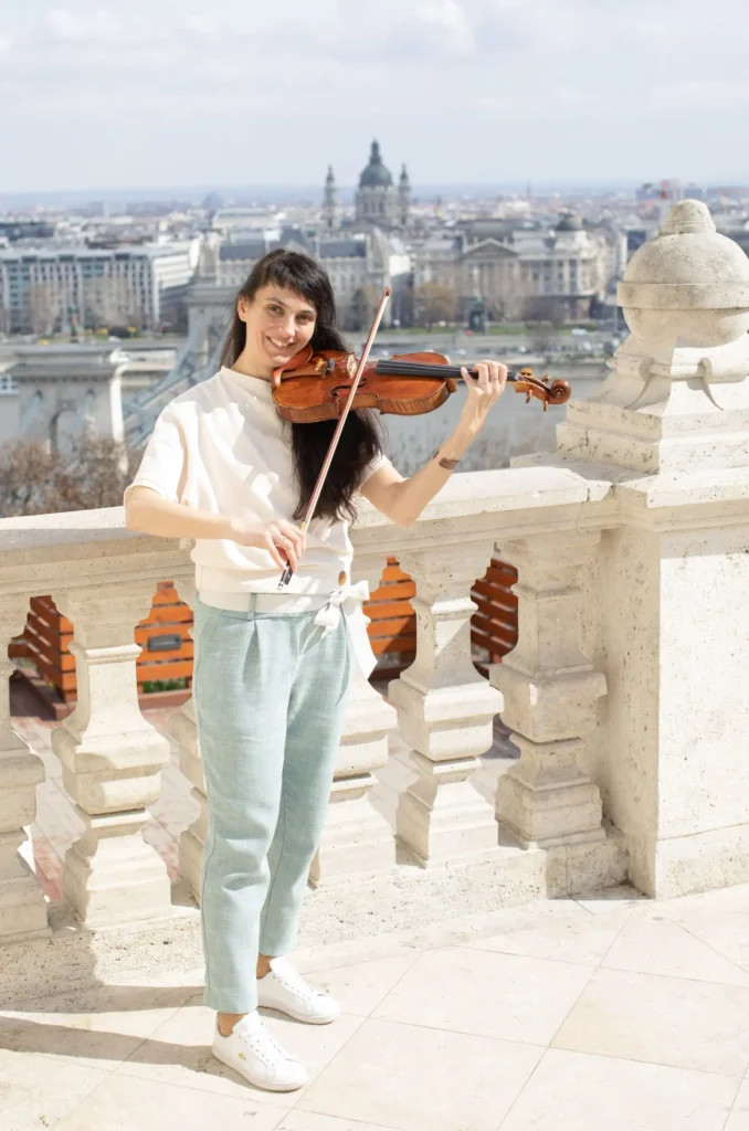 Annus Kriszta hegedül háttérben a parlamenti panoráma